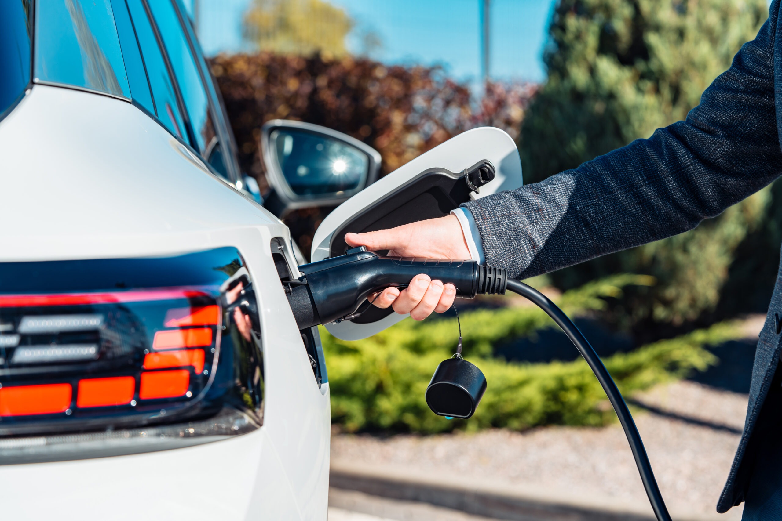 Electric car charging. Man's hand inserting the electrical connector to the electric car. Green energy, eco friendly fuel.