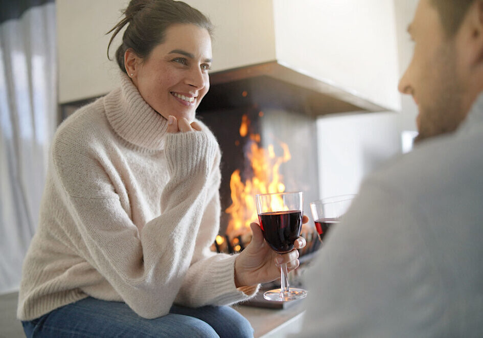Couple relaxing by the fire enjoying glass of red wine